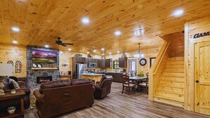 A cozy cabin interior with a living room, fireplace, kitchen, and a staircase leading to a loft bedroom.