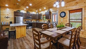 A cozy cabin-style kitchen with wooden walls, a central island with seating, and a dining area with a table and chairs.