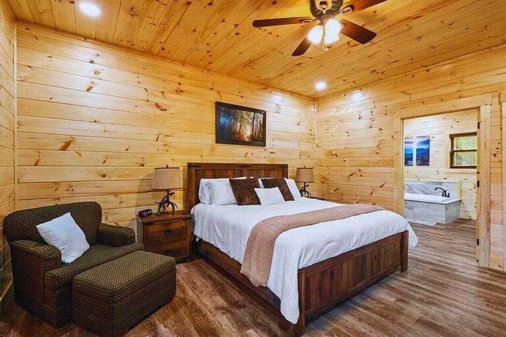A wooden-paneled bedroom with a bed, nightstands, a chair, and a ceiling fan.