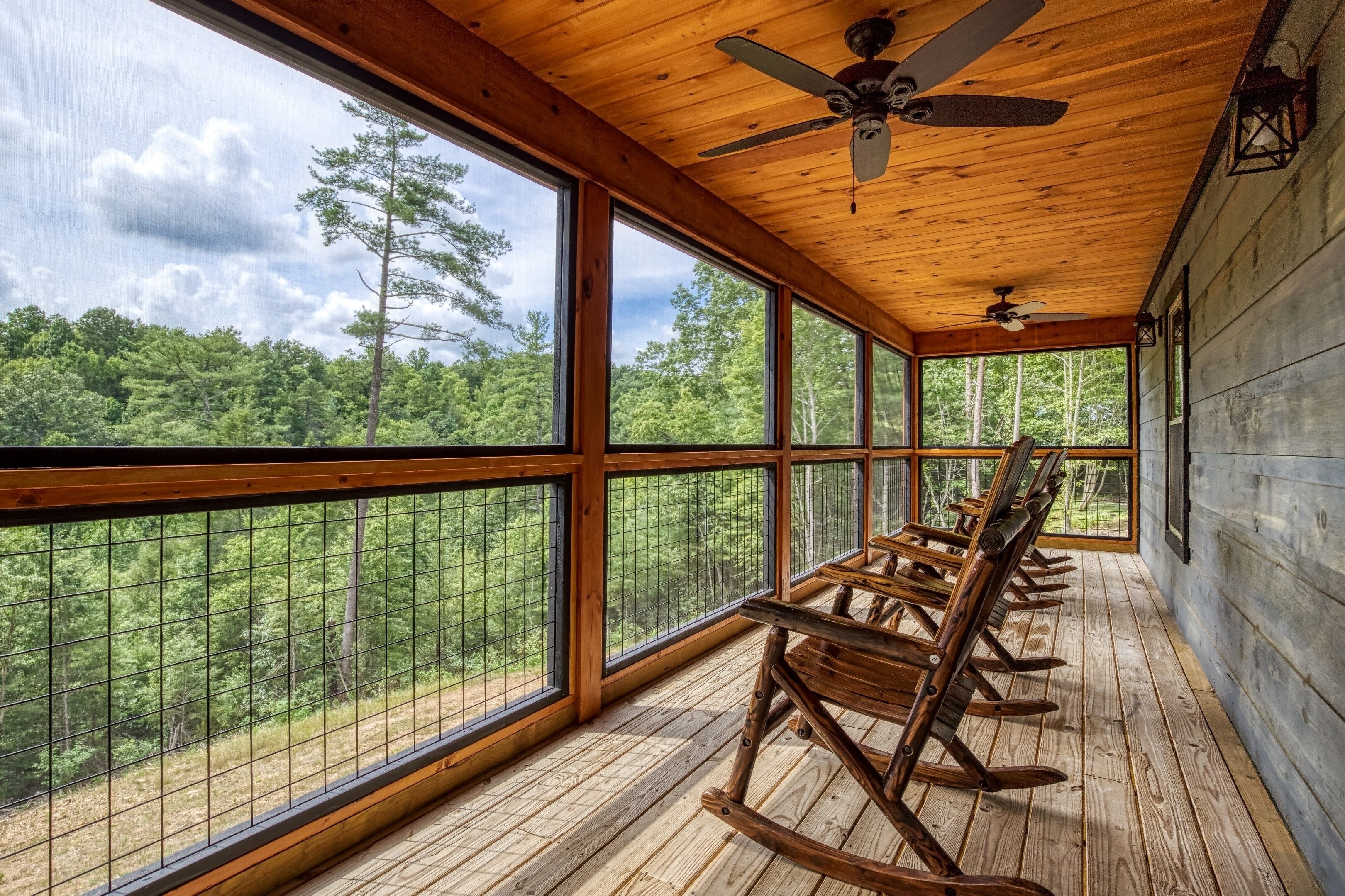 Eine Holzterrasse mit Schaukelstühlen und großen Fenstern mit Blick auf einen Wald.