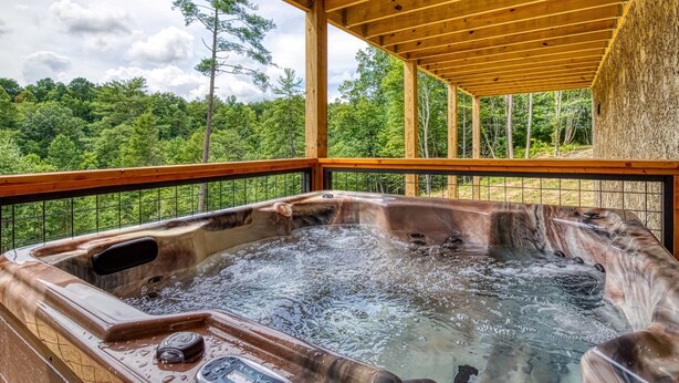 A hot tub under a wooden pergola with a view of a forested area.