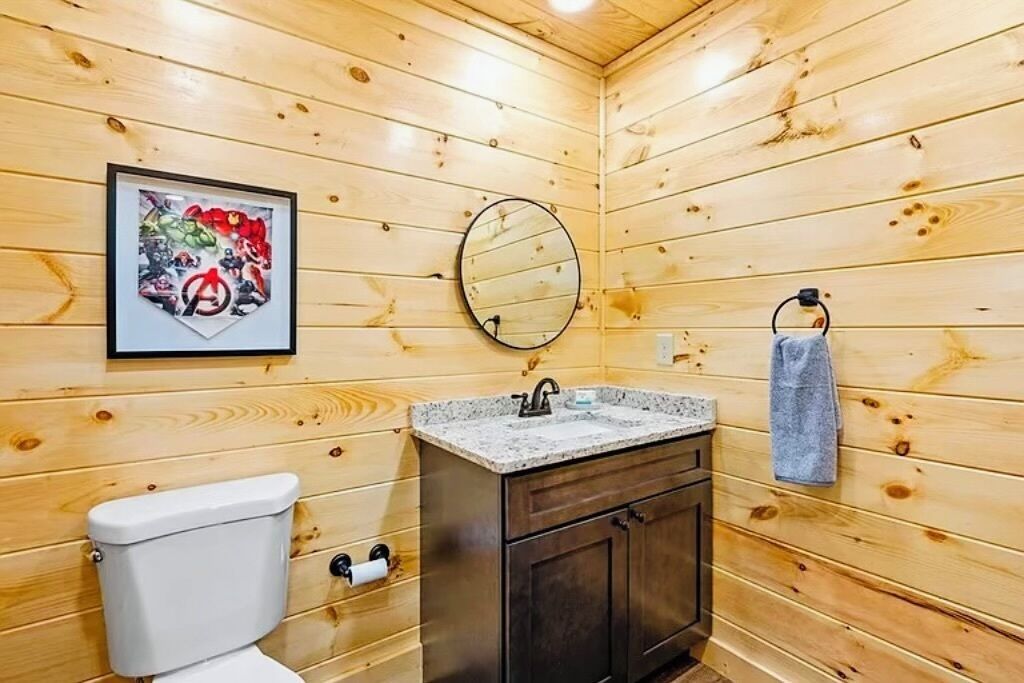 A wooden-paneled bathroom with a toilet, sink, and a framed picture on the wall.