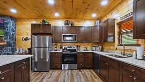 A modern kitchen with wooden cabinets, stainless steel appliances, and a stone accent wall.