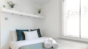 A neatly made bed with white and teal bedding, a pair of rolled towels, and a window with a view of the outside. - London Flat in the Heart of Fitzrovia (London)