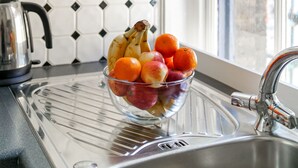 A kitchen with a clear glass bowl of fruit on the counter, a kettle, and a window with a view of a brick building. - London Flat in the Heart of Fitzrovia (London)