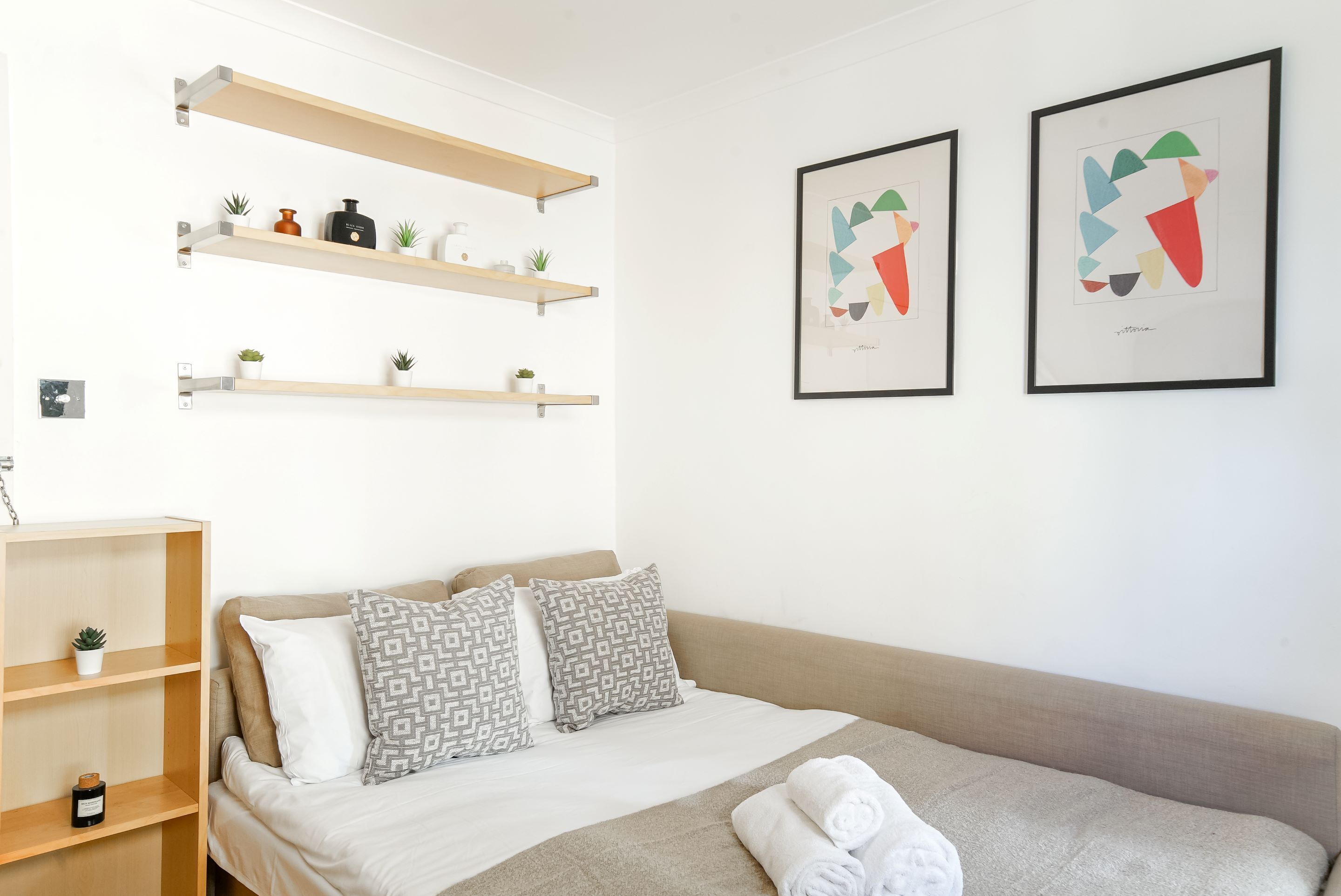 A neatly arranged bedroom with a bed, pillows, a blanket, and a shelf with decorative items.