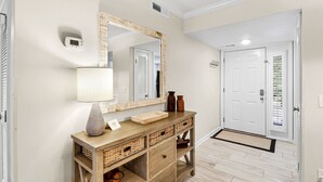 Un corridoio con una consolle in legno, uno specchio, una lampada e una porta con finestra.