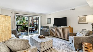 Un soggiorno con divano, poltrone, tavolino, televisore e un balcone con mobili da esterno.
