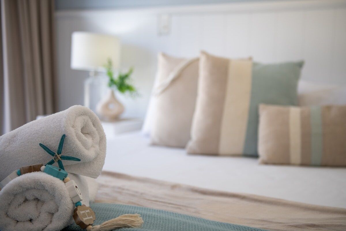 Cama bem arrumada com uma toalha enrolada e um objeto decorativo.