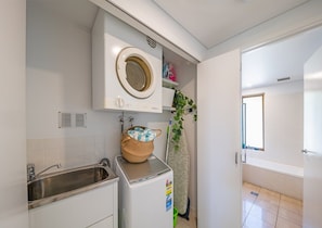 A compact kitchen with a built-in washing machine, a sink, and a window. - Kalani On Airlie (Airlie Beach)