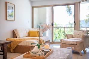 A cozy room with a bed, a wicker chair, a tray with a candle, and a window with a view. - Kalani On Airlie—Scenic Views near Marina (Airlie Beach)