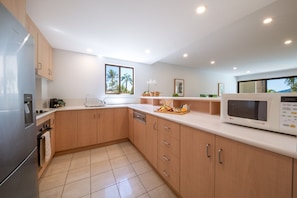 A modern kitchen with a refrigerator, microwave, and wooden cabinets. - Kalani On Airlie (Airlie Beach)