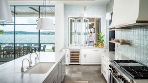 Una cocina moderna con un amplio ventanal que da a una masa de agua, estufa integrada y vistas al área del patio exterior.