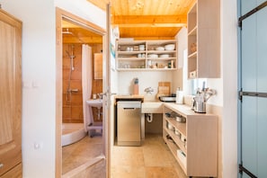 A compact kitchen with a dishwasher, wooden shelves, and a shower area.