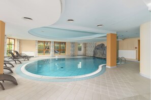 A large indoor swimming pool with clear blue water, surrounded by tiled flooring and equipped with several lounge chairs. - Schwarzer Adler (Nauders)