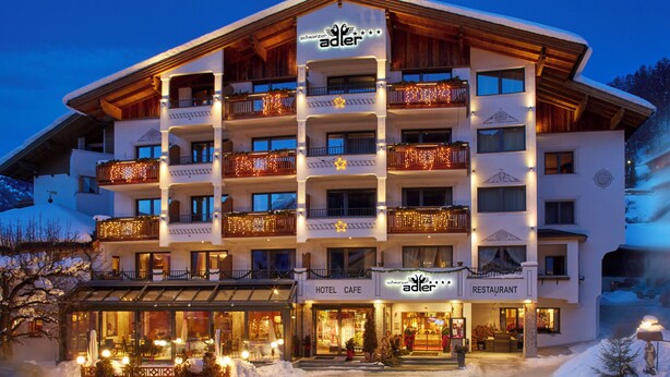 A multi-story hotel with balconies adorned with lights, a cafe, and a restaurant. - Schwarzer Adler (Nauders)