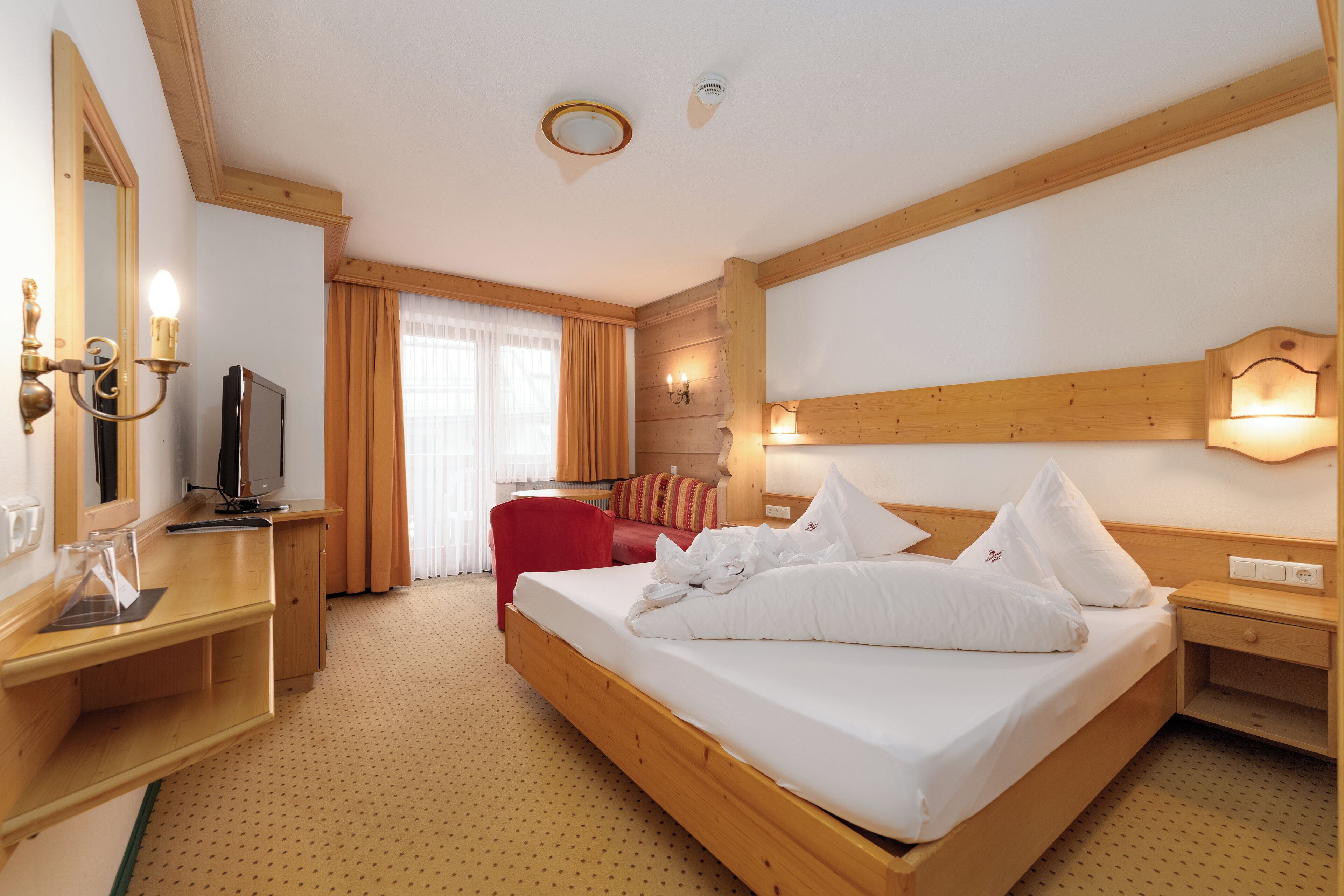 A hotel room with a wooden bed, a TV, a desk, and a chair.