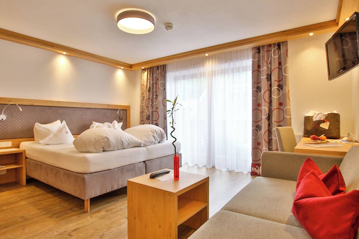 Habitació d'hotel moderna amb un llit, una taula de nit de fusta, un vas vermell, un sofà i una televisió penjada a la paret.
