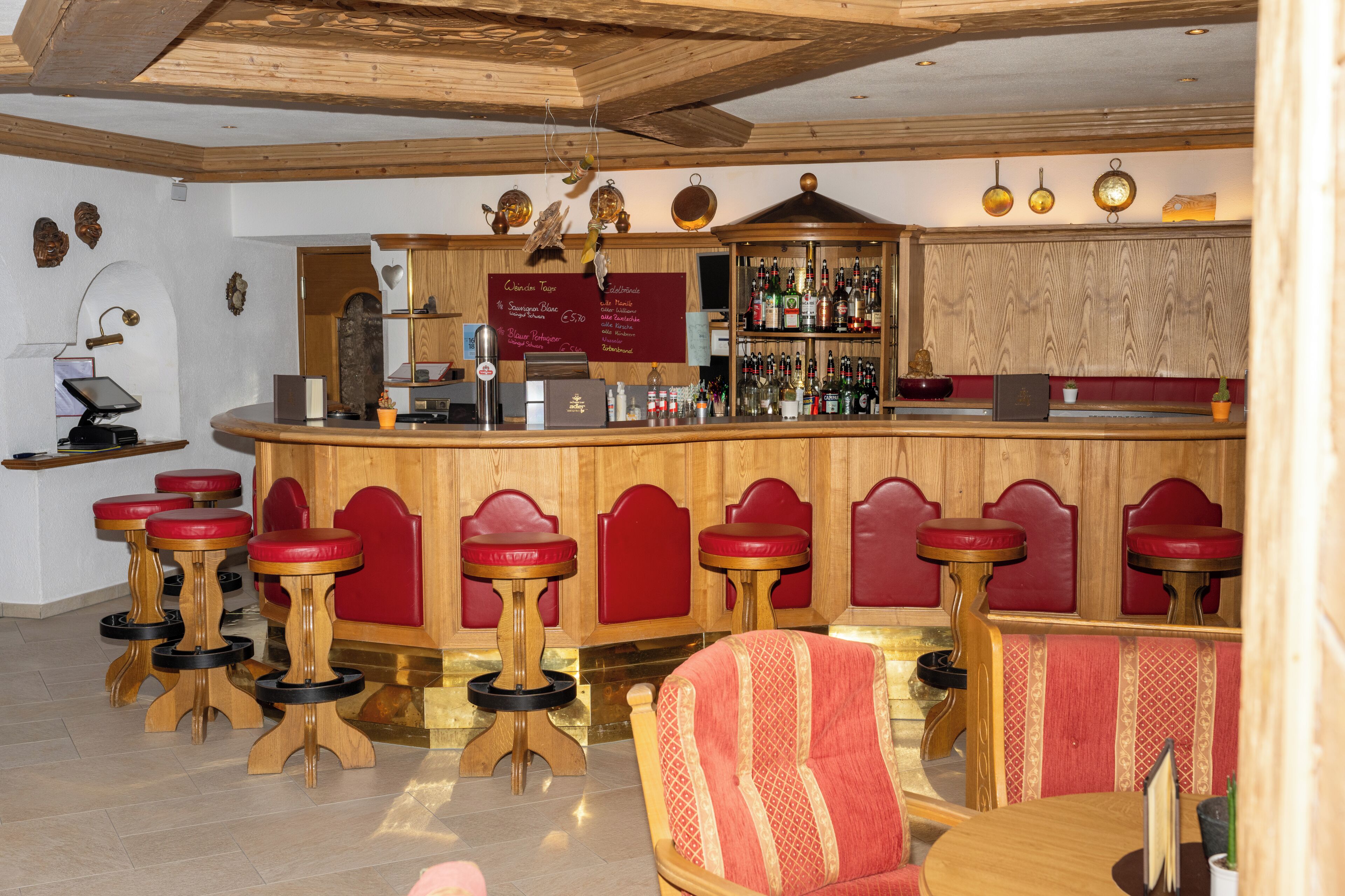 Un espace bar avec des tabourets de bar en bois, des chaises rembourrées de couleur rouge et un comptoir en bois sur lequel est affiché le menu.