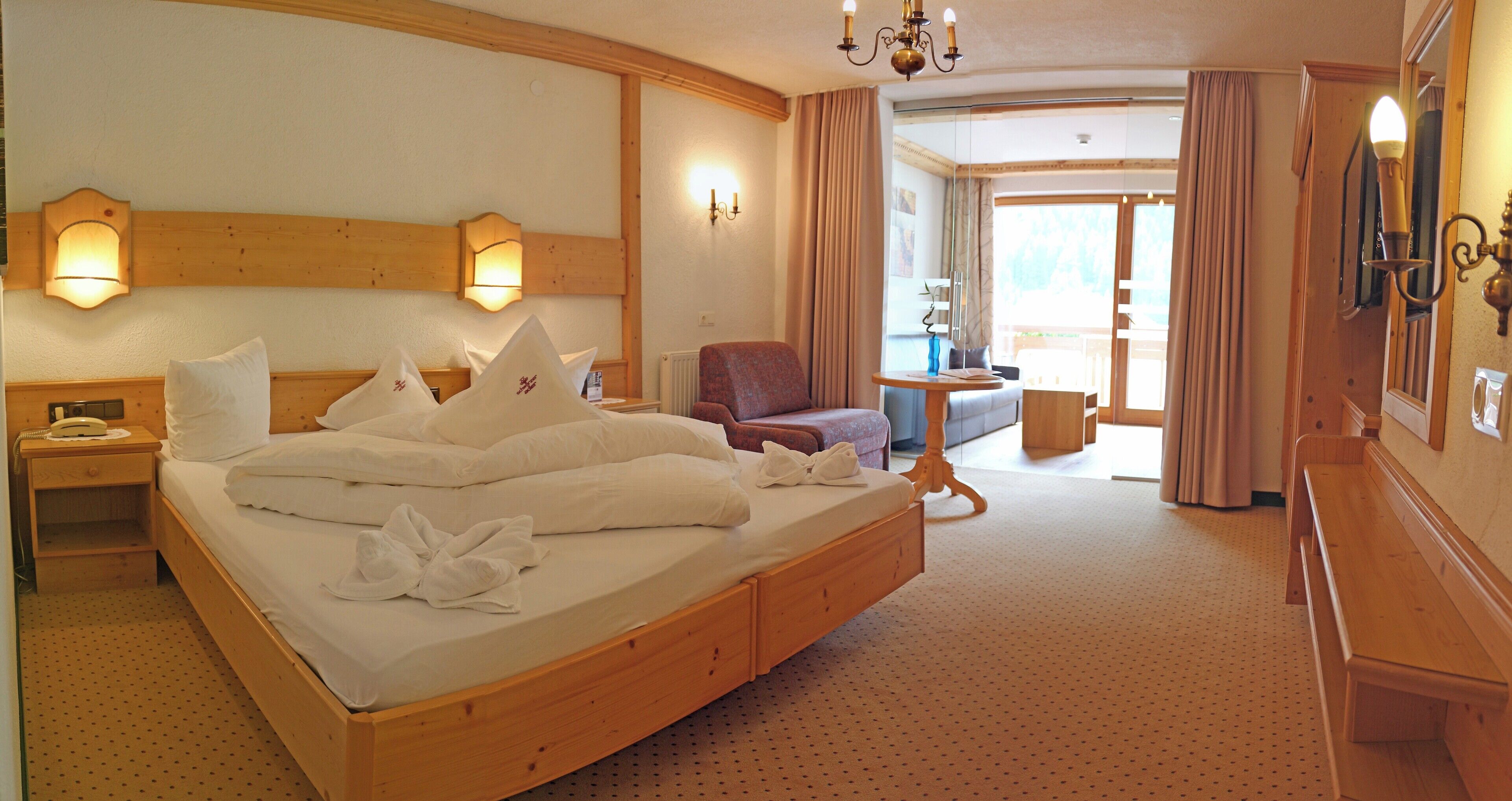 A hotel room with a large bed, a wooden headboard, a bedside table with a lamp, a chair, and a small table with a vase.