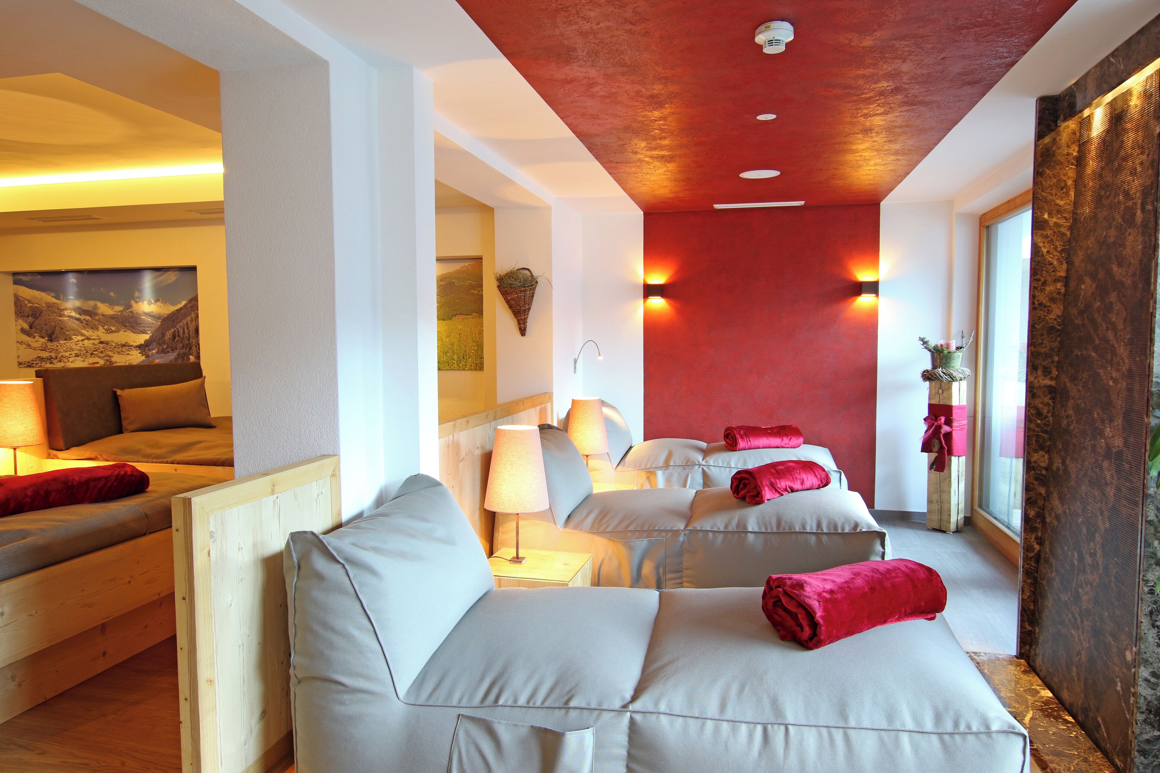 A hotel room with a wooden bed, a sofa, and a red accent wall.