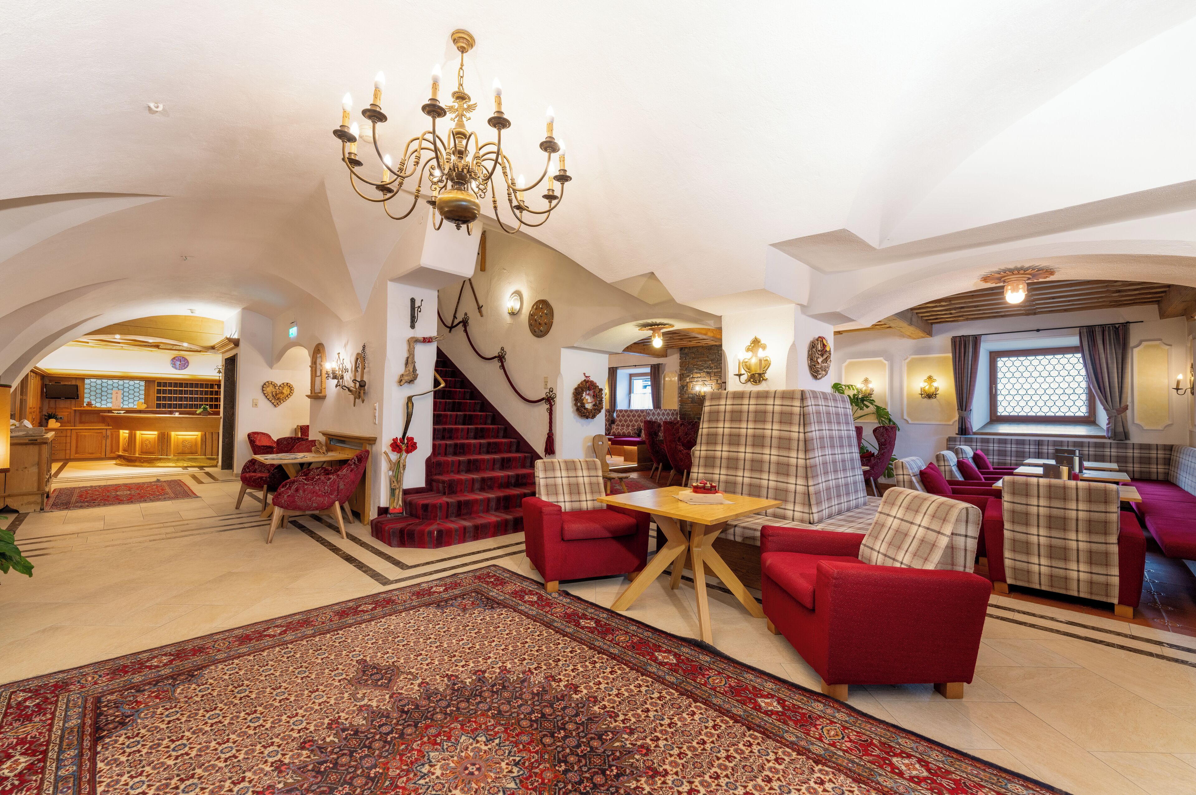 A spacious living area with red and beige furniture, a chandelier, and a staircase leading to another room.
