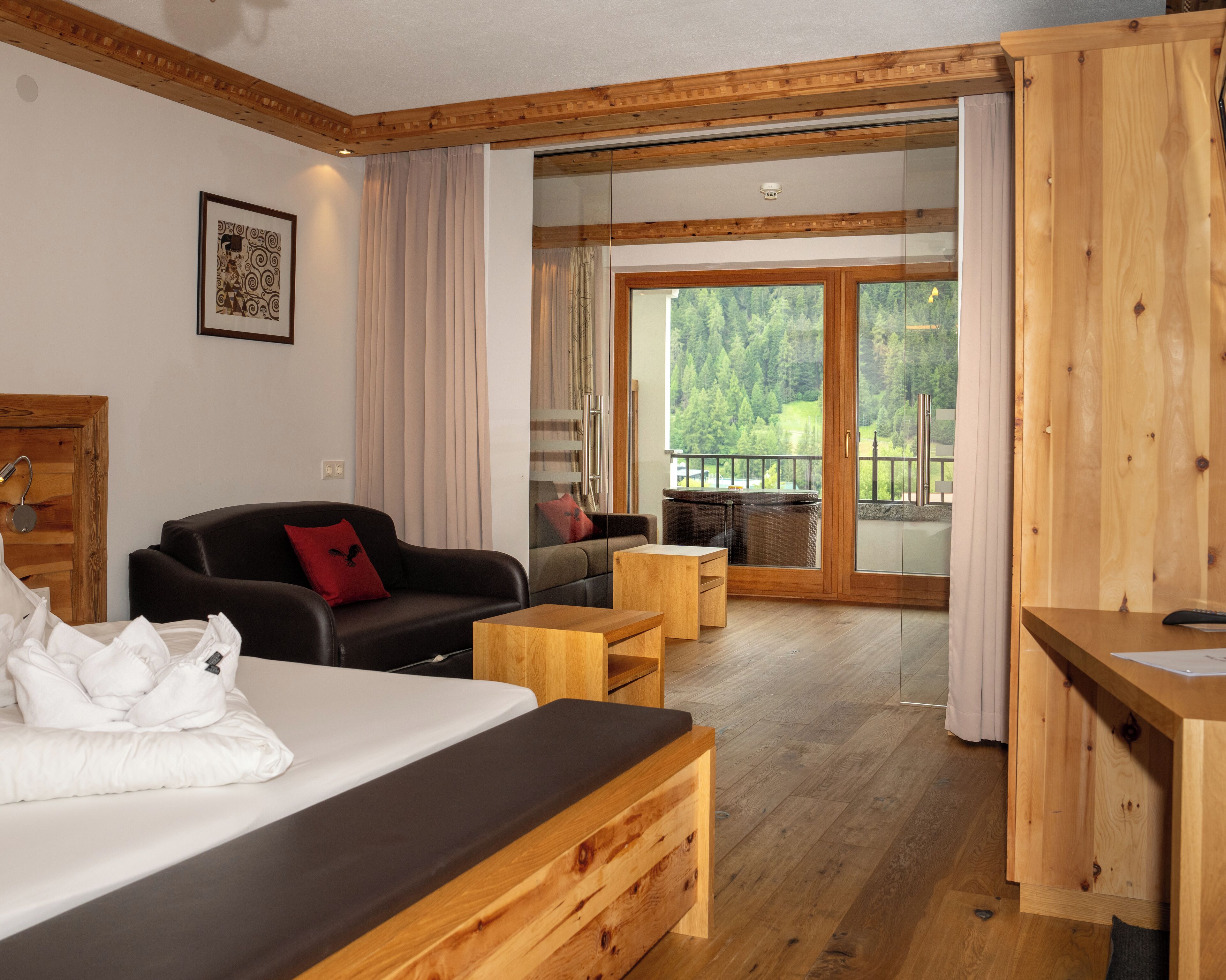 Quarto de hotel moderno com cama, sofá, uma mesinha e varanda com vista para a floresta.
