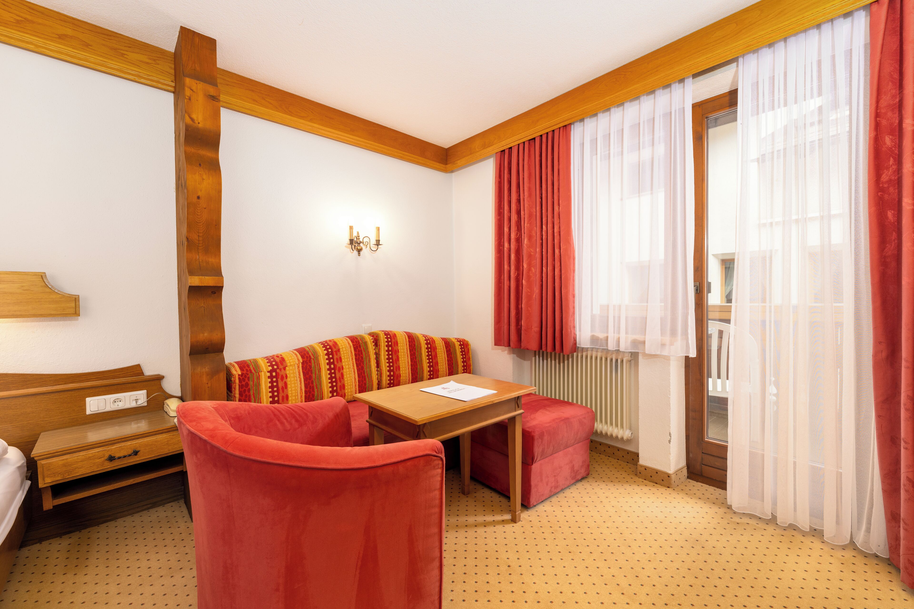 Una habitación con techo de madera, un sofá, una mesa y una ventana con cortinas rojas.
