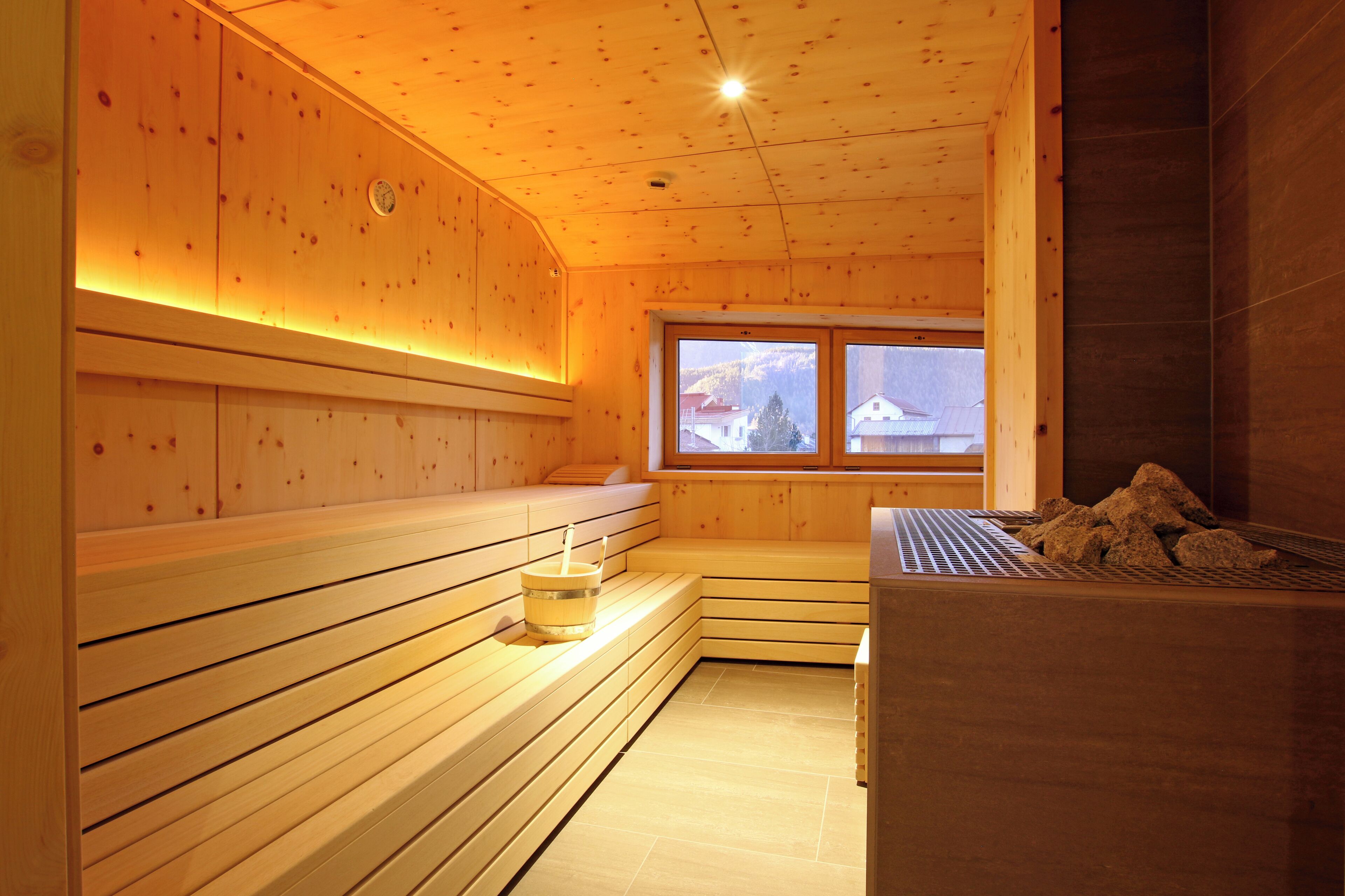 A wooden sauna with benches, a window with a view of mountains, and a sauna heater.