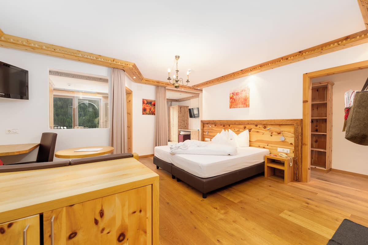 Habitació d'hotel amb llit de fusta, escriptori, televisió i finestra amb cortines.
