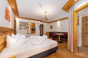 A hotel room with a large bed, wooden headboard, a small dining table, a sofa, and a glass door leading to a shower area. - Schwarzer Adler (Nauders)