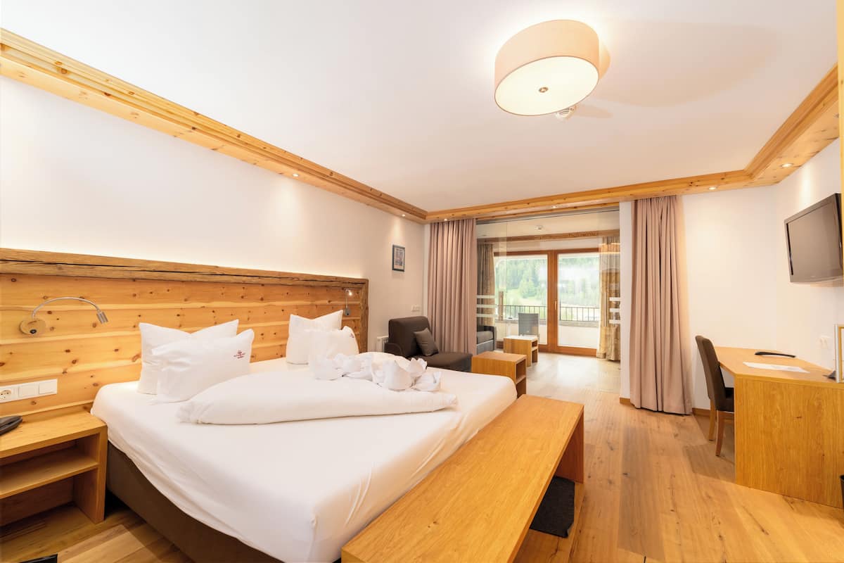 Habitació d'hotel amb capçal de llit de fusta, un llit gran amb roba de llit blanca, una taula de treball amb una cadira, una panxa i una televisió.