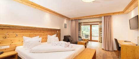 Habitación de hotel con cabecera de madera, una cama grande con ropa blanca, un escritorio con una silla, un banco y un televisor.