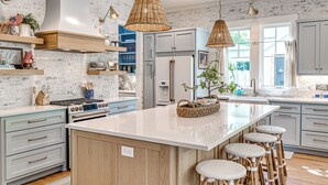 Una cocina moderna con una isla grande, taburetes de bar y una lámpara colgante.