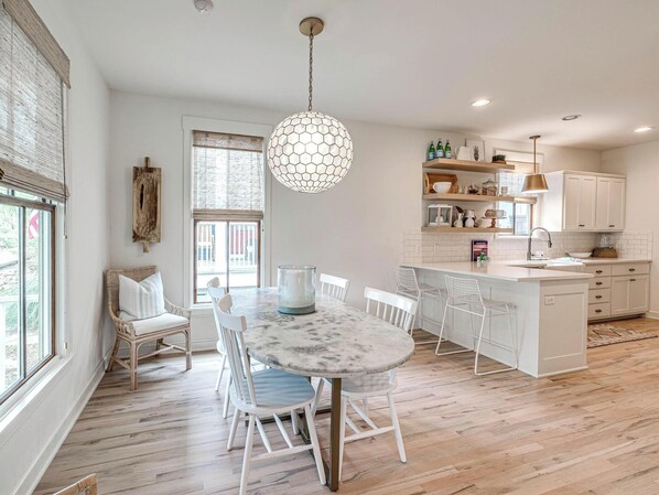 A modern kitchen with white cabinetry, a marble island, and a hanging hexagonal light fixture.