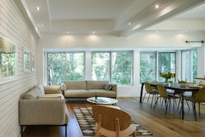 A spacious living area with a sofa, chairs, a dining table, and large windows offering a view of trees. - Country Vibes in Tel-Aviv by Sea N' Rent (Tel Aviv)