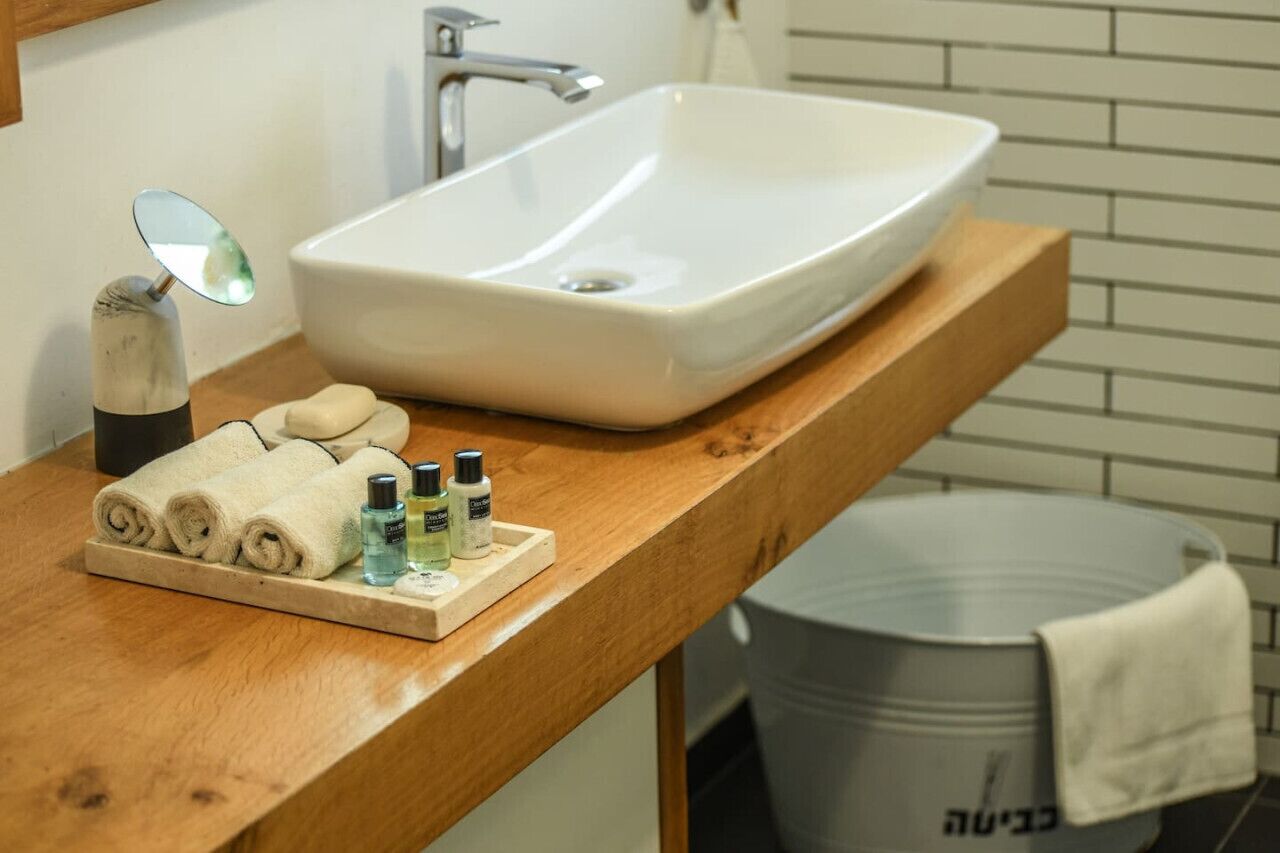A bathroom with a white sink, a wooden countertop, a mirror, and toiletries.