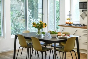 Ein Essbereich mit einem Tisch für vier Personen, einer Vase mit Sonnenblumen und einer Küchenarbeitsfläche mit Obst.