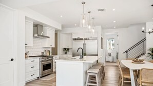 A modern kitchen with white cabinetry, stainless steel appliances, and a central island with stools. - Sunstone: Desert Color Lagoon + Beaches (St George)