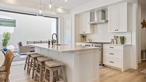 A modern kitchen with white cabinetry, a central island with stools, a stove, and pendant lighting. - Sunstone: Desert Color Lagoon + Beaches (St George)