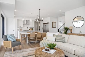 A modern living room with a sofa, a coffee table, and a dining area with chairs and a kitchen in the background.