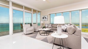 A spacious living room with a large window overlooking a scenic view, a ceiling fan, and a modern coffee table. - Brand New Phoenix Gulf Tower Now Open! (Orange Beach)