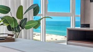 Una habitación con un ventanal que da a una playa, una planta en el alféizar y un mueble para televisión.