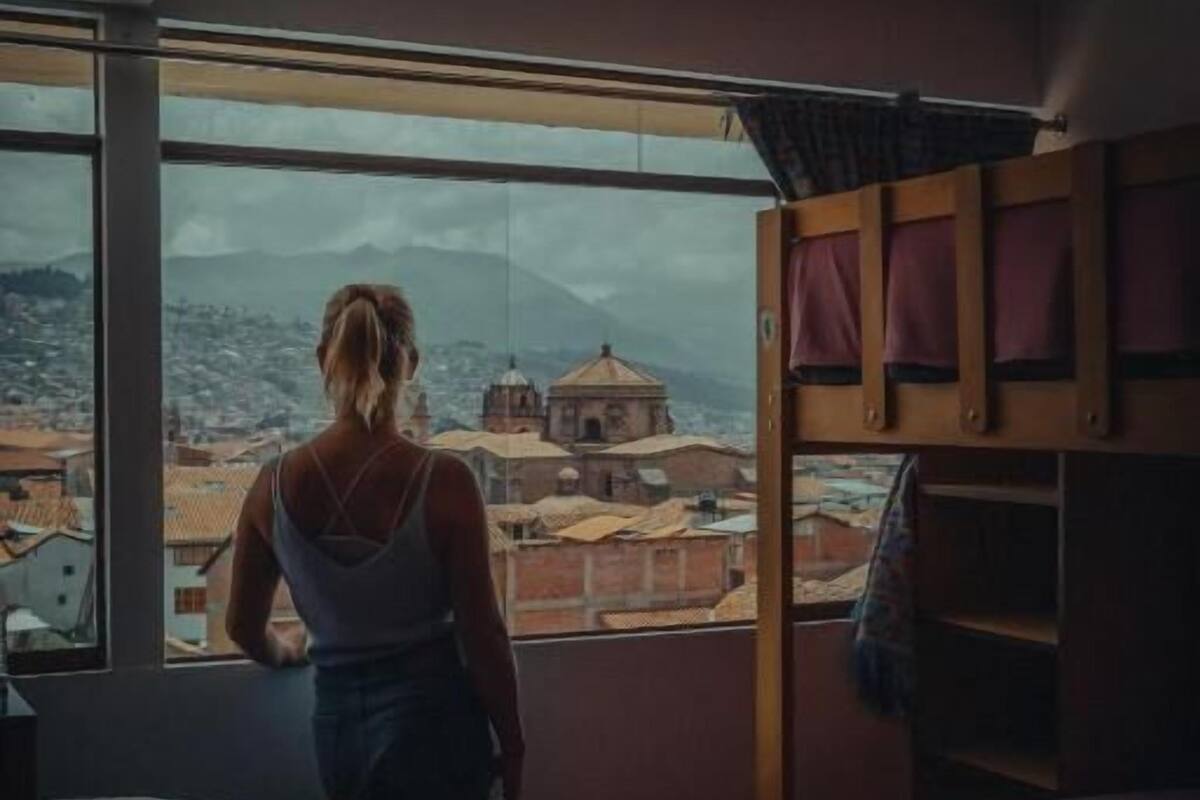 A room with a large window overlooking a cityscape, bunk beds, and a bed with a red blanket.