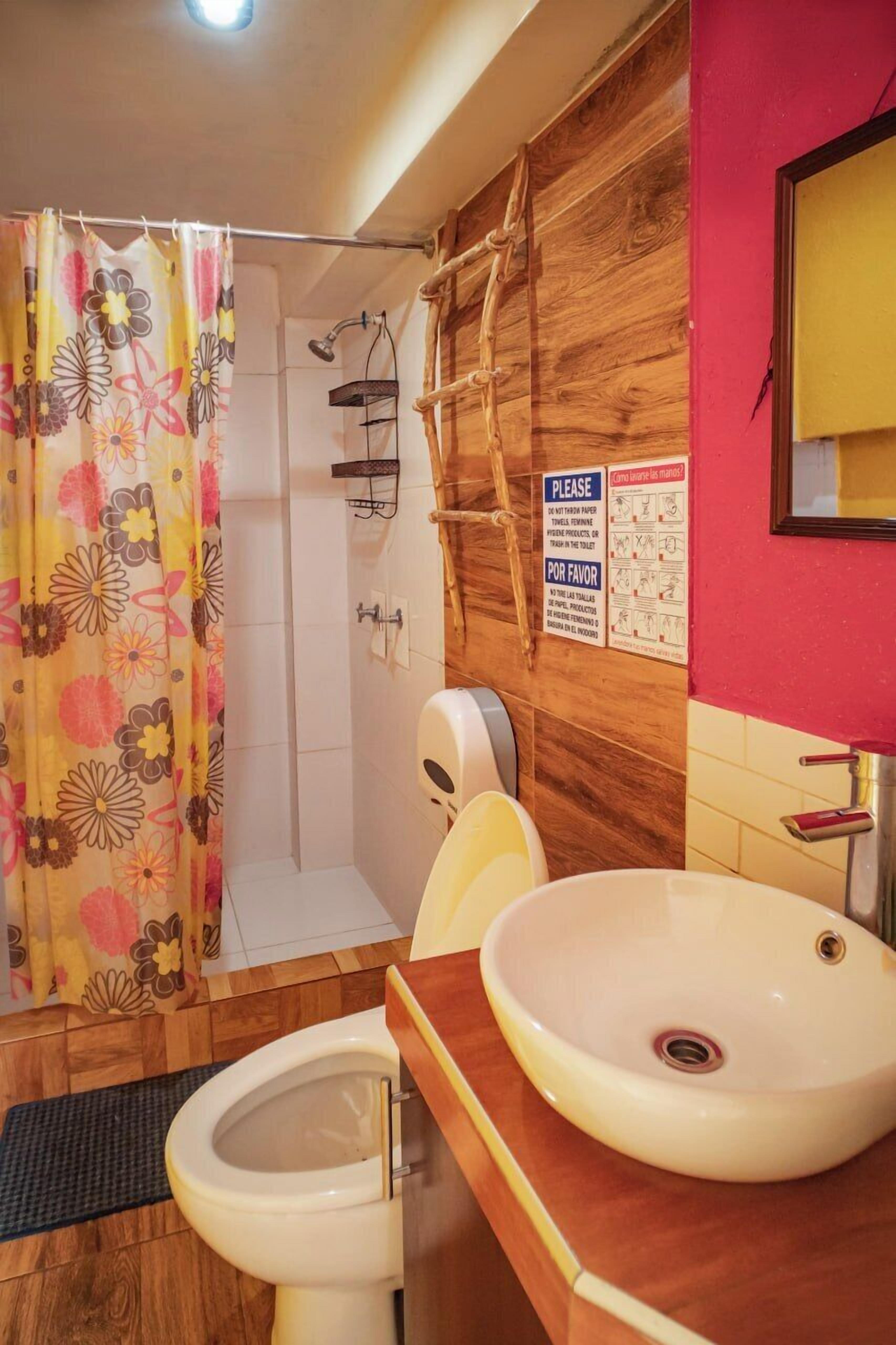 A bathroom with a toilet, sink, shower, and a wooden wall with a sign.