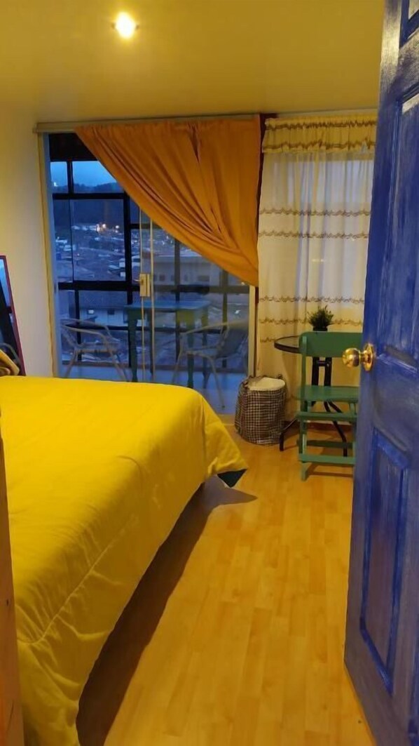 Una habitación con cama, ventana con cortinas, una mesita y una silla.