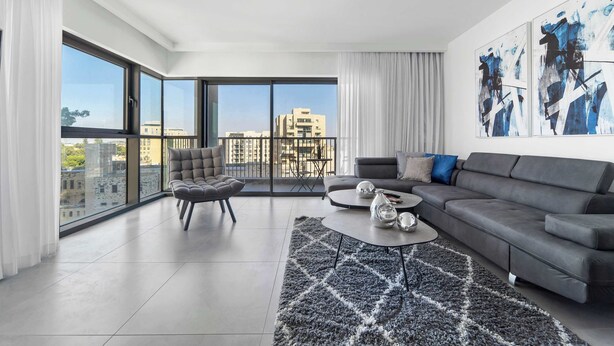 A modern living room with a grey sofa, a round coffee table, and a large window offering a city view. - Tranquil 2Bdr Oasis In The Heart Of Jerusalem (Jerusalem)
