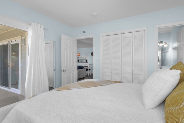 A bedroom with a large bed, white curtains, and a sliding glass door leading to a balcony. - Beach Birds: Oceanfront Condo with Excellent Views (Oak Island)