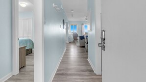 Een gang met een houten vloer, een bed met een blauw beddegoed, een stoel en een bureau met een computer.