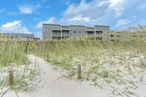 A modern building with multiple balconies, surrounded by sand and tall grasses. - Beach Birds: Oceanfront Condo with Excellent Views (Oak Island)